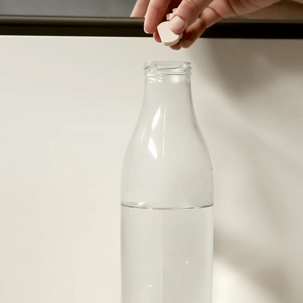 Main plaçant une pastille de shampoing en bouteille d'eau pour chien, biodégradable et hydratante, avec argile rose et huile essentielle.