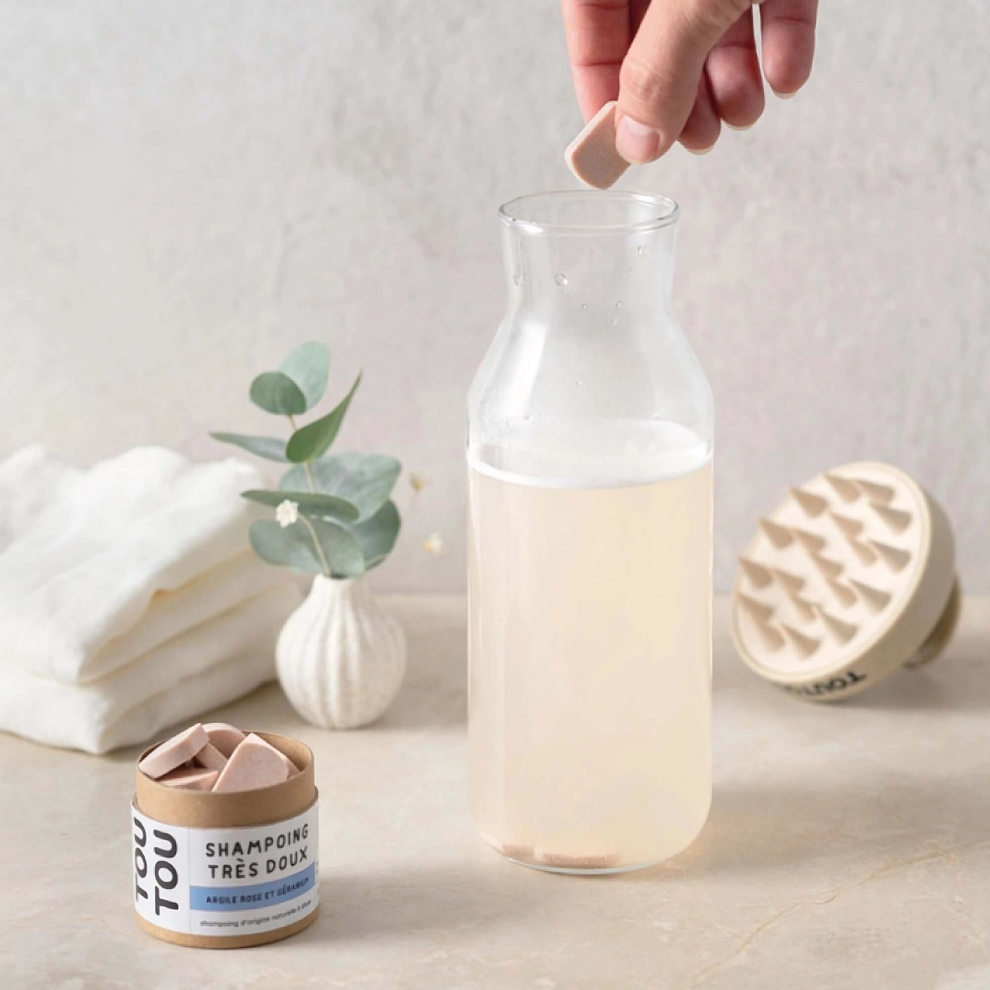Pastille de shampoing pour chien biodégradable dans un flacon, avec boîte, serviettes et plante, pour poils doux et hydratés.