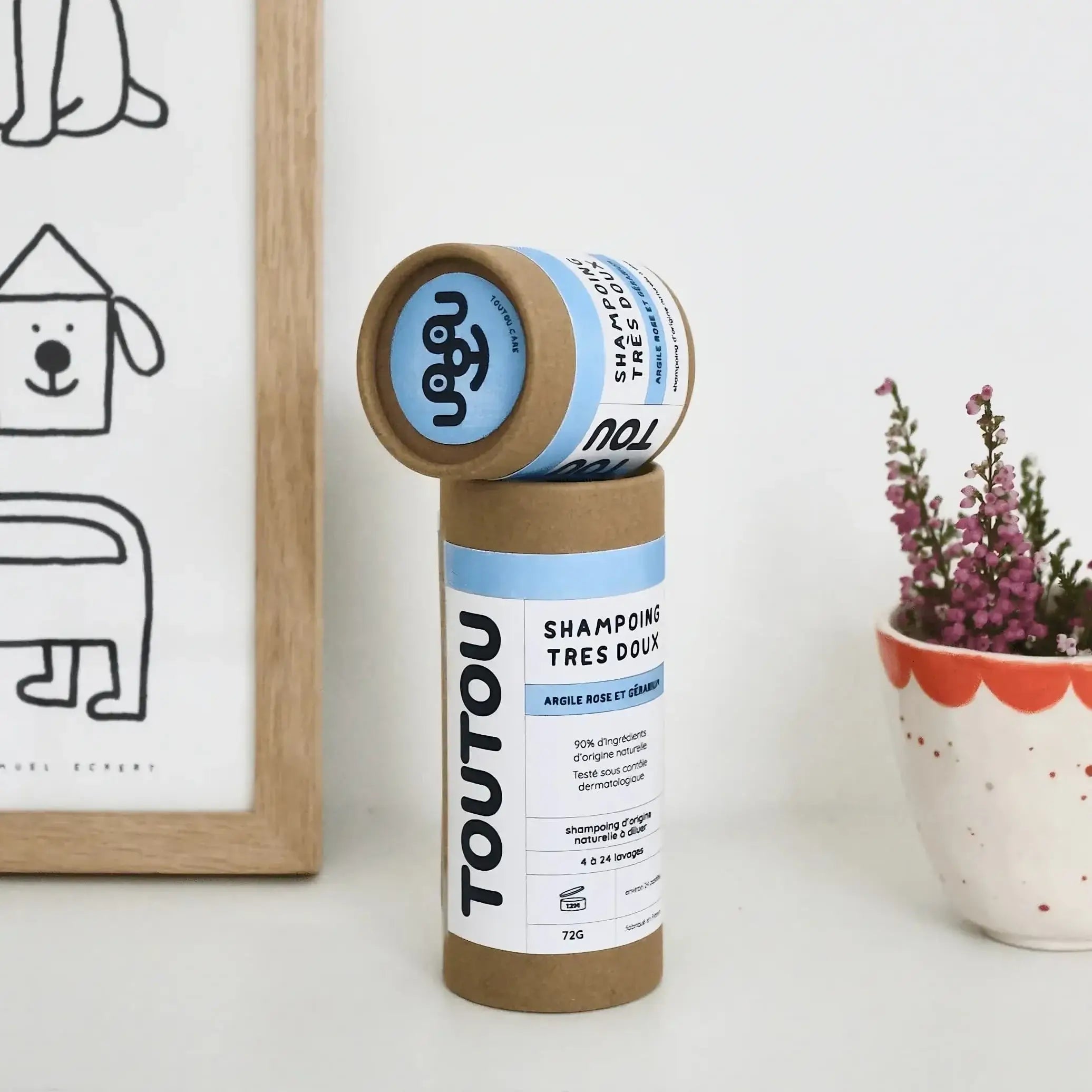 Toucan tube de shampoing en pastilles pour chien avec argile rose et huile essentielle de géranium, posé sur une table à côté d'une plante.